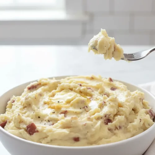 Close-up of creamy garlic mashed potatoes featuring roughly chopped red potatoes boiled and mashed with butter, garnished with black pepper and pieces of cooked red potato skins. Melted butter pools on the surface creating a glossy sheen.