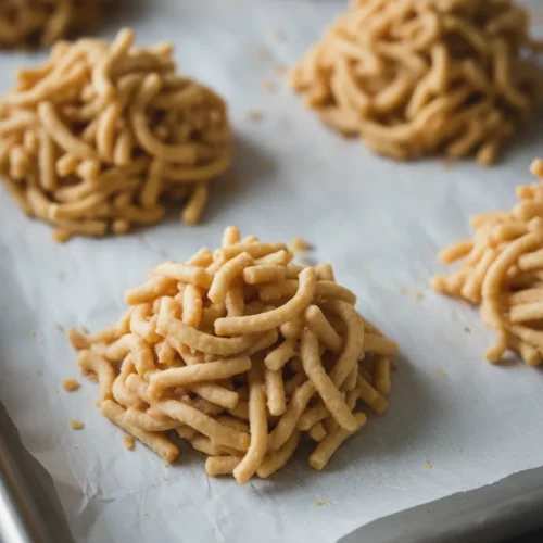 Clusters of haystack cookies made with chow mein noodles coated in a light caramel-colored butterscotch, arranged on parchment paper on a metal baking sheet.