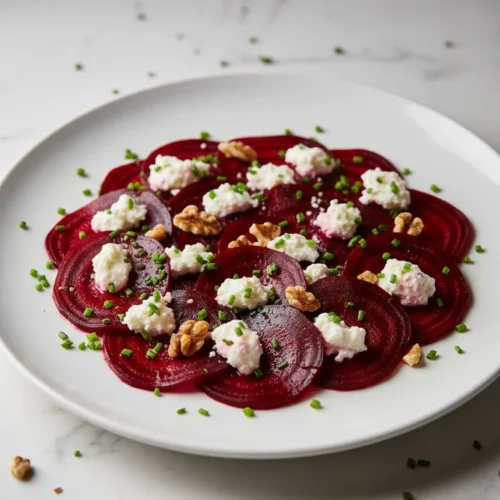 Roasted beets with goat cheese salad featuring thinly sliced beets, crumbled goat cheese, chopped walnuts, and a garnish of chives, set against a bright white background.