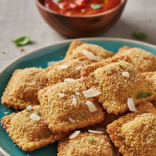 Crispy toasted ravioli on a turquoise plate. The ravioli are golden-brown with an evenly distributed breadcrumb coating, sprinkled with parmesan cheese. Forks are placed amongst the ravioli, set against a rustic textured backdrop.