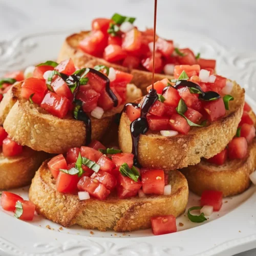 Close-up of bruschetta with tomato basil, featuring toasted bread topped with diced tomatoes, fresh basil, and balsamic glaze on a white ornate platter.