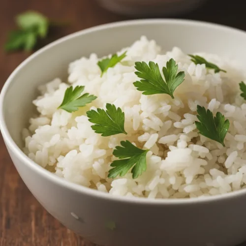 A bowl of garlic butter rice topped with fresh parsley. The rice is fluffy and glistening, with each grain distinct. The bowl is white ceramic and sits on a dark brown wooden surface.