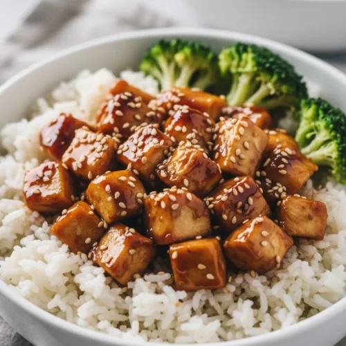 A bright, appetizing teriyaki chicken bowl featuring diced chicken pieces glazed with teriyaki sauce, sprinkled with sesame seeds, served with fluffy rice and green broccoli florets.