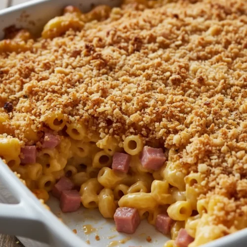 Partially eaten corned beef casserole featuring macaroni and cheese with a toasted breadcrumb topping. The creamy macaroni pasta has pieces of ham mixed in, and the breadcrumbs are toasted golden-brown. The dish is in a white ceramic baking dish.