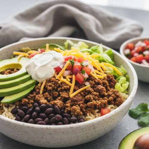 A vibrant and inviting healthy turkey taco bowl featuring cooked ground turkey, black beans, shredded cheddar cheese, creamy avocado slices, a dollop of sour cream, fresh pico de gallo, crisp lettuce, and fluffy rice, arranged artfully in a speckled ceramic bowl.