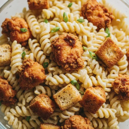 Overhead close-up shot of a generous serving of creamy Chicken Bacon Ranch Pasta Salad with turkey bacon, featuring rotini pasta, crispy chicken pieces, and green onions in a clear bowl.