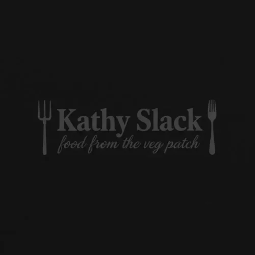 Minimalist logo for 'Kathy Slack - food from the veg patch' featuring a stylized pitchfork and fork framing typography, inspired by grape juice ice cream aesthetics. The logo is monochromatic charcoal gray on a black background.
